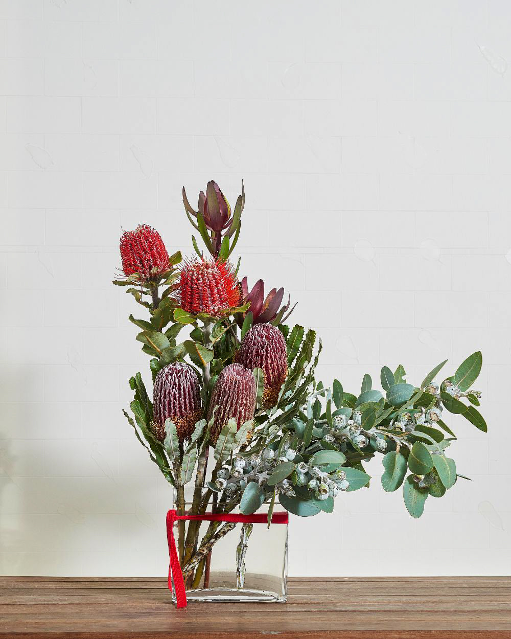 Textured vase arrangement overflowing with varied eucalyptus foliage, featuring decorative gum nuts.