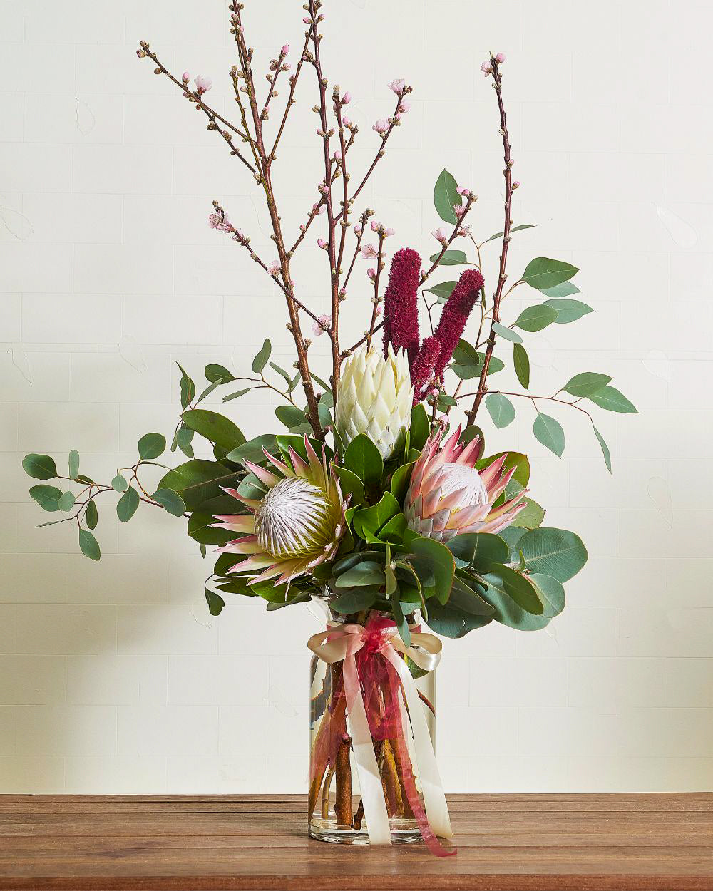 Large, majestic pink King Protea dominates the bouquet, accented by eucalyptus leaves and smaller native blooms.